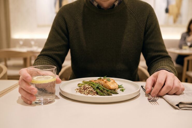 Tensión y control de movimientos al comer Primer plano de las manos de un hombre en una mesa con un platillo de pescado y un vaso de agua con limón.