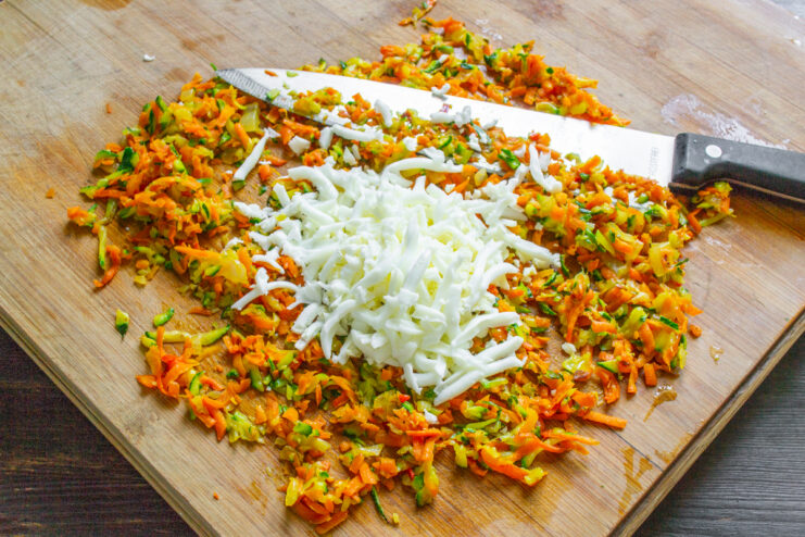 Mezcla de vegetales y huevo Huevo duro rallado agregándose al picadillo de vegetales en una tabla