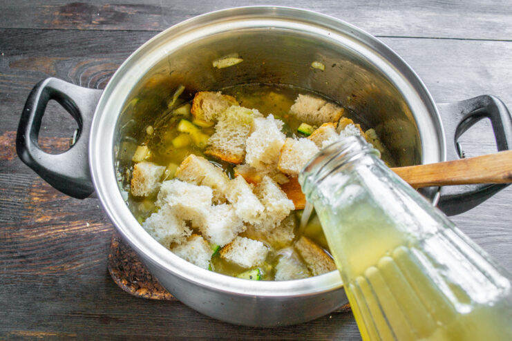 Adición del caldo a la olla Caldo de pollo vertiéndose en una olla con verduras y trozos de pan.
