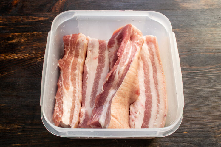 Acomodar la carne en el recipiente Trozos de panceta de cerdo acomodados dentro de un recipiente plástico