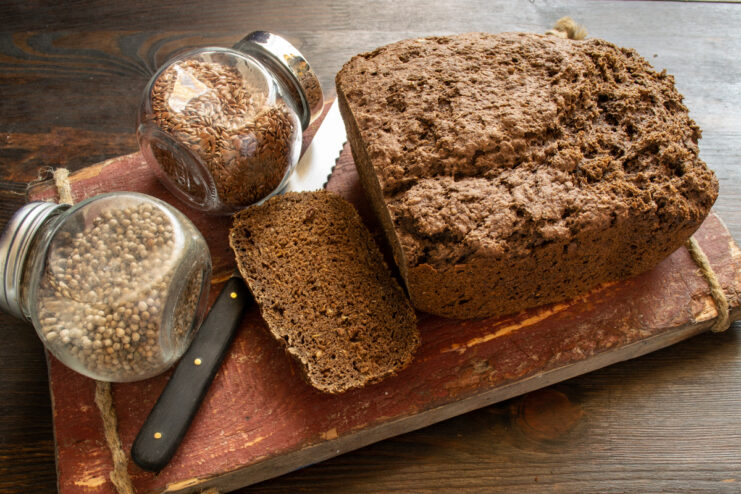 Presentación del pan Rebanada de pan de linaza en una tabla junto a frascos de especias
