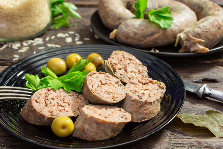 Rodajas de salchicha de hígado casera con arroz servidas en un plato decorado con aceitunas y perejil fresco.