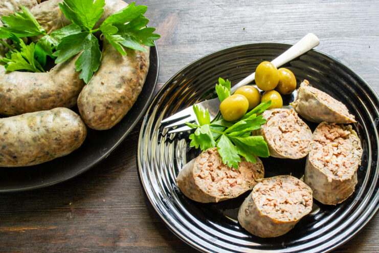 Rebanadas perfectas de salchicha de hígado presentadas en un elegante plato negro con aceitunas.