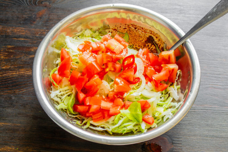 Cubos de tomate rojo recién cortados añadidos al repollo y cebolla.