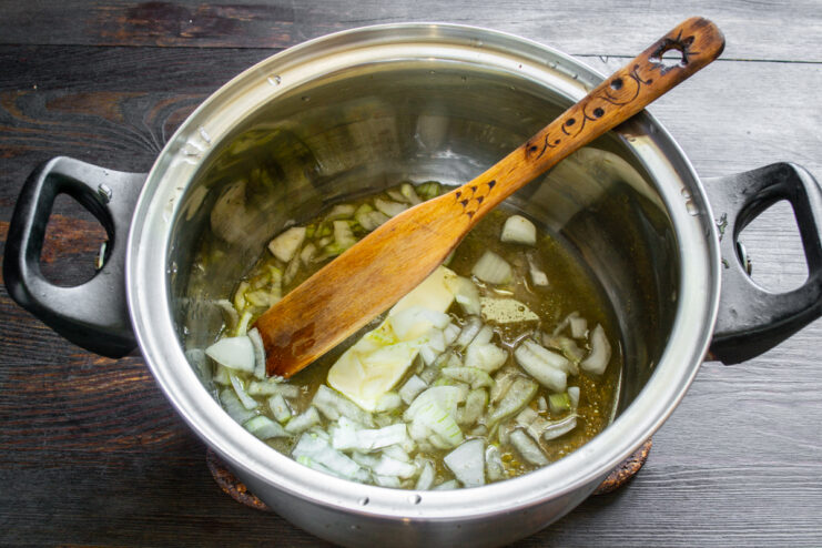 Sofrito de la cebolla Cebolla picada sofriéndose con mantequilla y caldo en una olla de acero inoxidable.