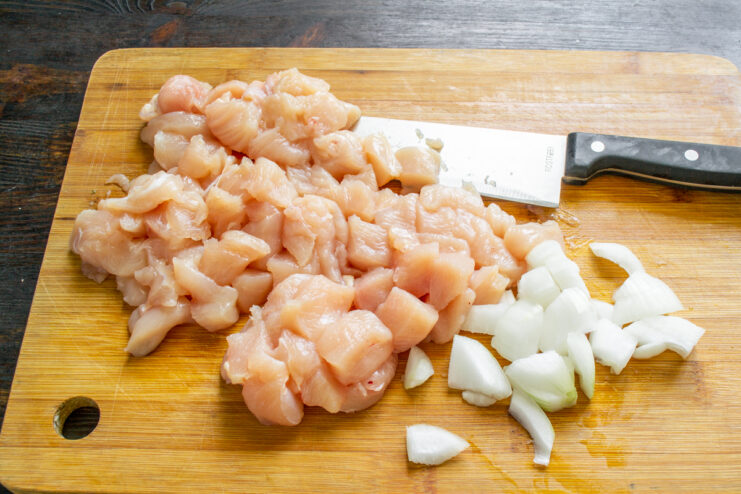 Añadiendo la cebolla Cebolla picada junto a los cubos de pollo crudo