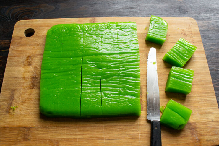 Corte en porciones Cortando la barra de dulce de manzana verde en cuadrados uniformes con un cuchillo.