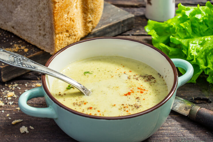 Sopa picante de zucchini con crema servida en un tazón azul sobre una superficie de madera.