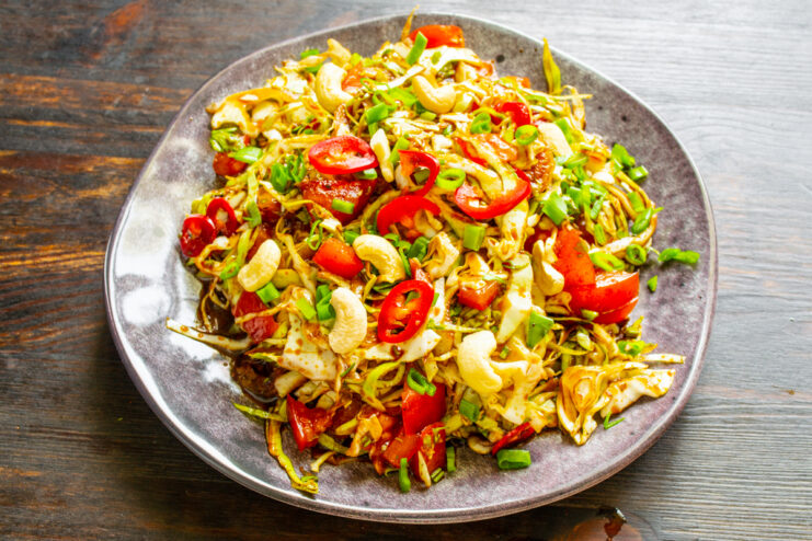 Plato extendido con ensalada de repollo, tomate y nueces de la India.