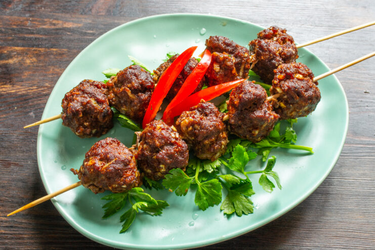 Presentación de albóndigas en brochetas con pimiento rojo y hierbas
