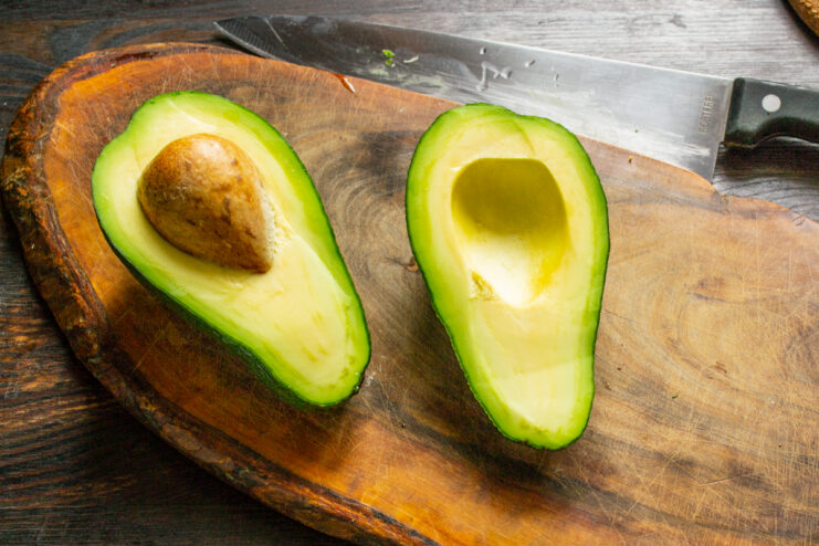 Preparación del aguacate Aguacate maduro cortado por la mitad sobre una tabla de madera