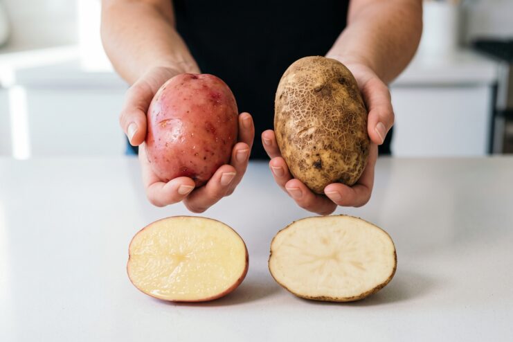 Papas cerosas y harinosas cortadas por la mitad Comparación de papa roja cerosa y café harinosa cortadas a la mitad sobre una mesa blanca