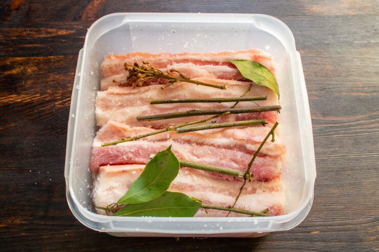 Adición de hierbas aromáticas Carne de cerdo en un recipiente junto con ramas de laurel fresco