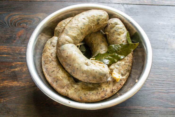 Salchicha de hígado cocida enfriándose en un recipiente junto a unas aromáticas hojas de laurel.