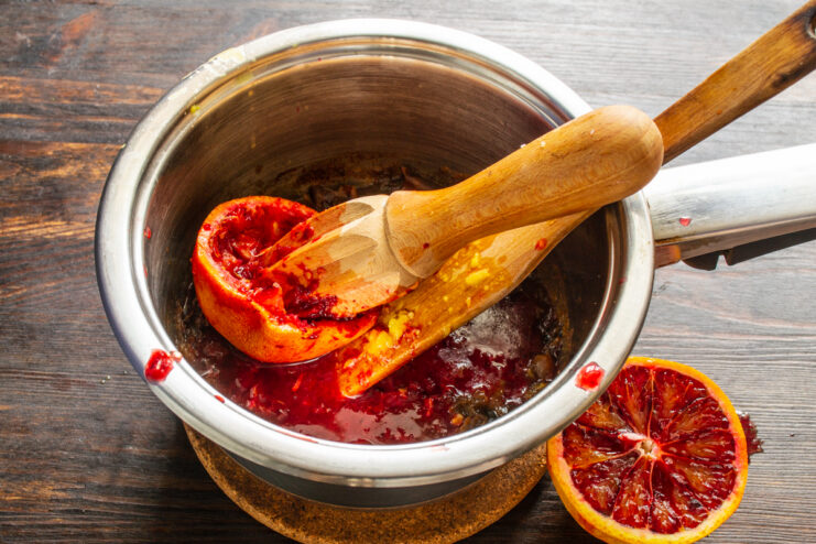 Agregando el jugo de naranja Exprimiendo jugo de naranja roja sobre los dátiles cocidos en la olla