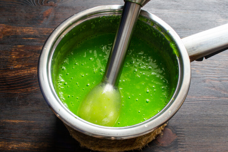 Batido del puré de manzana Batiendo la mezcla verde para gomitas con una licuadora de inmersión.