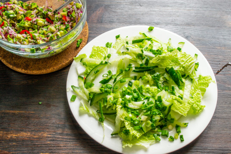 Agregando el cebollín a la ensalada Cebollín picado sobre la col y los pepinos en el plato